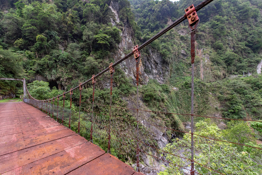 View of the suspension bridge at Taroko National Park surrounded by lush green mountains and rocky cliffs in Xiulin Township Hualien County Taiwan.