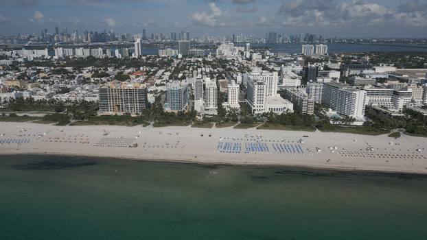 Aerial view of Miami Beach featuring the sandy shoreline rows of beach umbrellas and the urban skyline of high rise hotels in Miami Beach Florida United States. Aerial view of Miami Beach featuring the sandy shoreline rows of beach umbrellas and the urban skyline of high rise hotels in Miami Beach Florida United States.