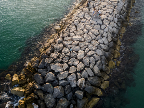 Aerial view of a stone breakwater with people standing on the rocks surrounded by turquoise sea water Sitges Catalonia Spain. Aerial view of a stone breakwater with people standing on the rocks surrounded by turquoise sea water Sitges Catalonia Spain.
