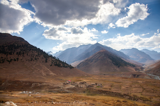 View of Astore Valley featuring a small village nestled among vast rugged mountain slopes under a dramatic cloudy sky in Astore Gilgit Pakistan. View of Astore Valley featuring a small village nestled among vast rugged mountain slopes under a dramatic cloudy sky in Astore Gilgit Pakistan.