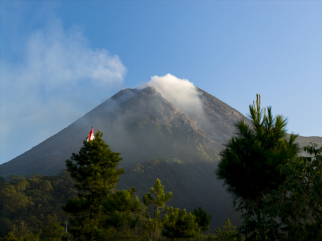 Aerial view of Mount Merapi with smoke rising from the crater and lush pine trees in the foreground in Kecamatan Pakem Daerah Istimewa Yogya Indonesia. Aerial view of Mount Merapi with smoke rising from the crater and lush pine trees in the foreground in Kecamatan Pakem Daerah Istimewa Yogya Indonesia.