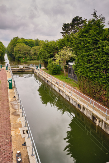 Wieringerwerf Netherlands 17 May 2026 View of Gemaal Leemans lock system with concrete walls metal railings and lush green trees under a cloudy sky.