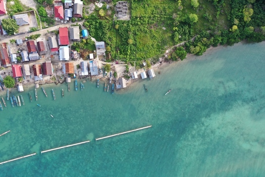 Aerial view of Pulau Maginti featuring a coastal village with colorful rooftops wooden boats moored along the shoreline and clear turquoise waters in Maginti South East Sulawesi Indonesia.