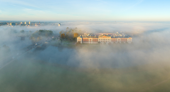 Aerial view of Jelgava Palace surrounded by thick morning fog with a bridge over the Lielupe River and the city skyline in the distance in Jelgava Latvia. Aerial view of Jelgava Palace surrounded by thick morning fog with a bridge over the Lielupe River and the city skyline in the distance in Jelgava Latvia.