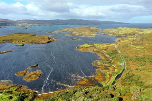 Aerial view of the rugged coastline and islands of Loch Dunvegan with a winding coastal road and lush green hills near Isle of Skye Scotland United Kingdom. Aerial view of the rugged coastline and islands of Loch Dunvegan with a winding coastal road and lush green hills near Isle of Skye Scotland United Kingdom.