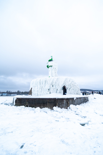 View of the frozen Molenfeuer Sassnitz lighthouse covered in thick ice and snow with people standing nearby on the icy pier in Sassnitz Mecklenburg Vorpommern Germany.