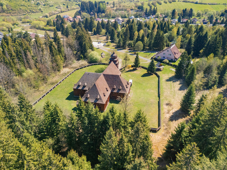 Aerial view of the Wooden Articular Church of Svaty Kriz surrounded by a wooden fence and lush green forest in Svaty Kriz Zilinsky kraj Slovakia.