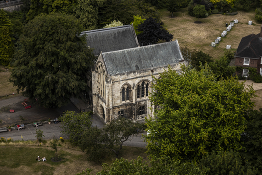 Aerial view of the historic St Mary s Abbey ruins surrounded by lush trees and parkland with people resting on benches in York England United Kingdom.