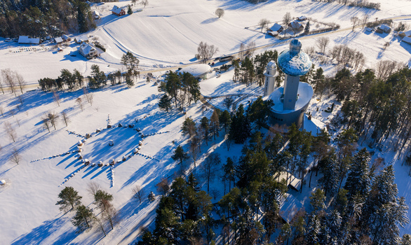 Aerial view of the Lithuanian Museum of Ethnocosmology featuring futuristic architecture with a glass sphere amidst a snow covered landscape and pine forests in Kulionys Utenos apskritis Lithuania.