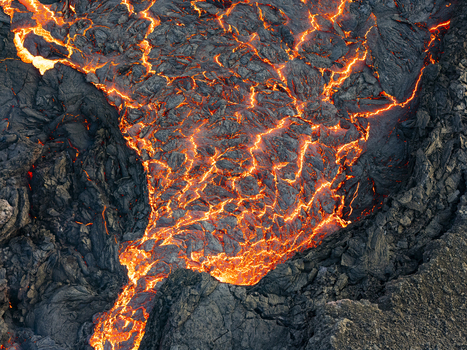 Aerial view of fiery lava flows through fractured cooling volcanic rock in Sundhn&uacute;kur Eruption Reykjanes Iceland.