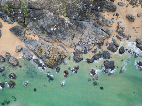 Aerial view of the rugged dark rocks and turquoise water at Godrevy Beach with sandy patches along the coastline in Gwithian England United Kingdom. Aerial view of the rugged dark rocks and turquoise water at Godrevy Beach with sandy patches along the coastline in Gwithian England United Kingdom.