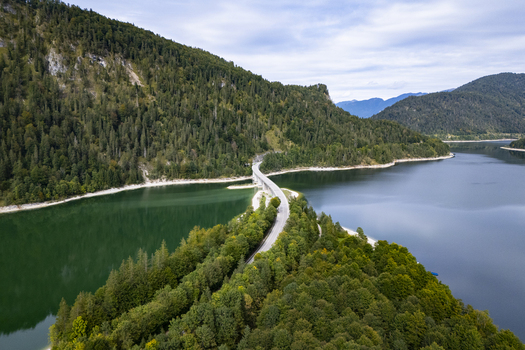 Aerial view of a bridge cutting through the tranquil waters of the Sylvensteinsee flanked by verdant forests under a serene sky Sylvensteinspeicher Bayern Germany. Aerial view of a bridge cutting through the tranquil waters of the Sylvensteinsee flanked by verdant forests under a serene sky Sylvensteinspeicher Bayern Germany.