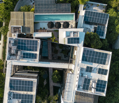 Aerial view of a modern building complex featuring extensive rooftop solar panels a turquoise swimming pool with black umbrellas and lush surrounding greenery in Merida Yucatan Mexico. Aerial view of a modern building complex featuring extensive rooftop solar panels a turquoise swimming pool with black umbrellas and lush surrounding greenery in Merida Yucatan Mexico.