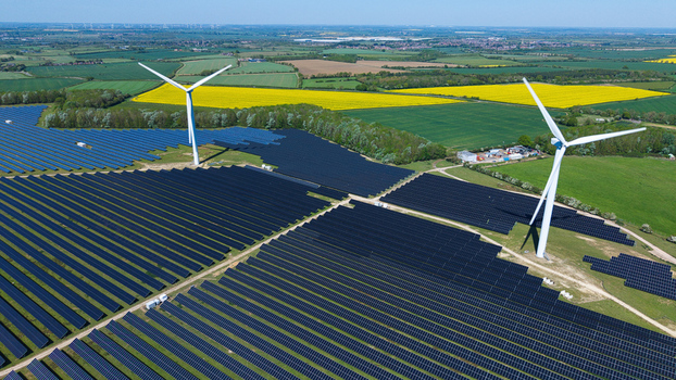 Aerial view of Chelveston Wind Farm featuring solar panels and wind turbines surrounded by green and yellow fields in Wellingborough England United Kingdom. Aerial view of Chelveston Wind Farm featuring solar panels and wind turbines surrounded by green and yellow fields in Wellingborough England United Kingdom.