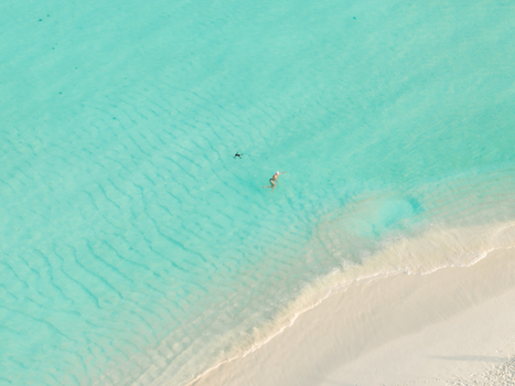Aerial view of the white sands meeting the turquoise waters with a swimmer enjoying the clear sea Dhidhdhoo Thiladhunmathi Atoll Maldives.
