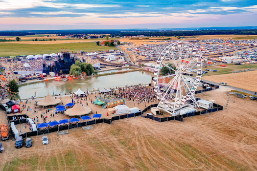 Herzogenaurach Germany 22 July 2022 Aerial view of the Open Beatz Festival featuring a large Ferris wheel music stages and crowds of people gathered in open fields during sunset. Herzogenaurach Germany 22 July 2022 Aerial view of the Open Beatz Festival featuring a large Ferris wheel music stages and crowds of people gathered in open fields during sunset.