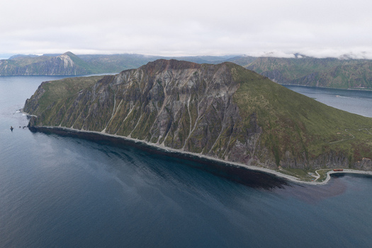 Aerial view of the rugged Mount Ballyhoo landscape with steep rocky cliffs lush green slopes and dark coastal waters in Unalaska Alaska United States.