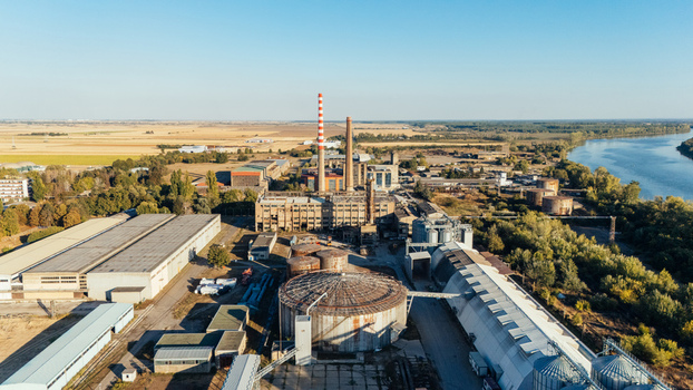 Aerial view of an industrial factory complex with tall chimneys storage tanks and warehouses situated near a river in Sremska Mitrovica Vojvodina Serbia. Aerial view of an industrial factory complex with tall chimneys storage tanks and warehouses situated near a river in Sremska Mitrovica Vojvodina Serbia.