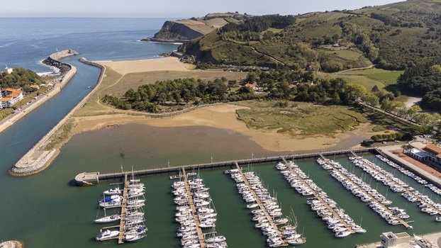 Aerial view of the marina in Zumaia with numerous boats docked at piers a breakwater sandy beach and lush green hills along the coast in Zumaia Basque Country Spain.