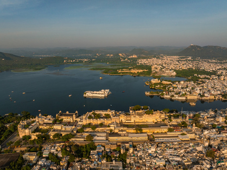 Aerial view of the City Palace complex and Lake Pichola with the Lake Palace in the distance surrounded by the historic urban landscape of Udaipur Rajasthan India.