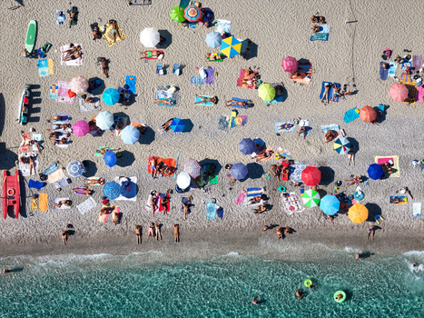 Aerial view of a public beach in Bergeggi Liguria Italy with colorful umbrellas sunbathers relaxing on the sand and clear turquoise water.