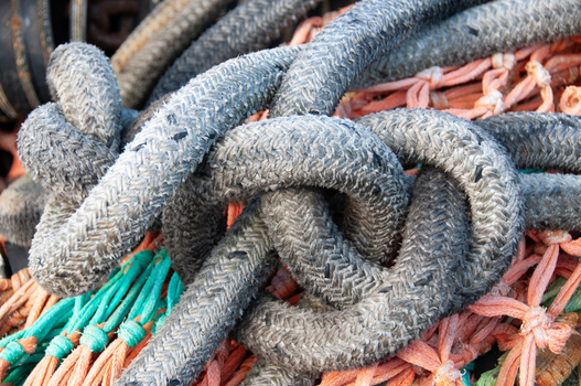 View of weathered nautical ropes knotted together on top of orange and teal fishing nets in Canada. View of weathered nautical ropes knotted together on top of orange and teal fishing nets in Canada.