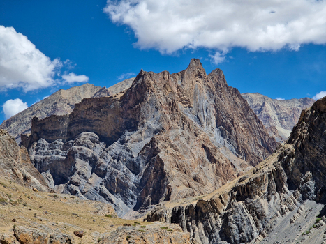 View of Penzi La road winding through the rugged rocky mountains of the Zanskar range under a bright blue sky with scattered clouds in Zanskar Ladakh India.