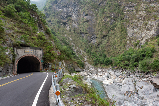 View of Taroko National Park featuring a road tunnel entrance carved into the rocky mountain gorge with a river flowing below in Xiulin Township Hualien County Taiwan.