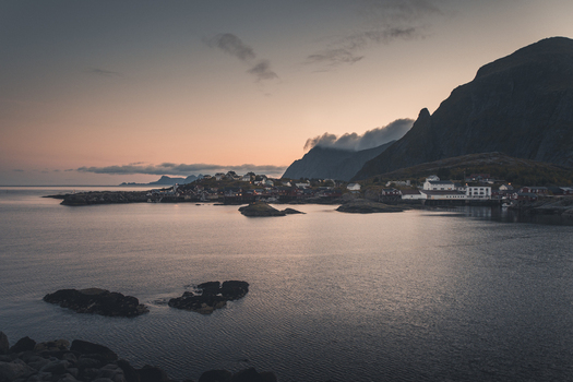View of the traditional fishing village of A with its iconic red wooden houses calm coastal waters and dramatic mountains under a soft twilight sky in A Nordland Norway.