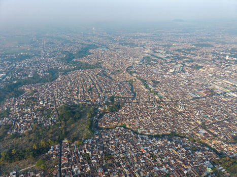 Aerial view of the dense urban landscape featuring tightly packed rooftops narrow streets and scattered green spaces under a hazy sky in Malang East Java Indonesia.