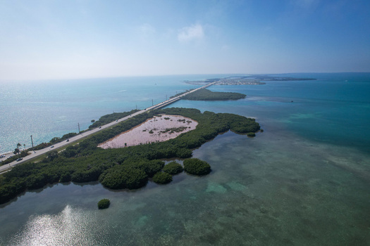 Aerial view of The Overseas Highway stretching across lush green mangrove islands and turquoise ocean waters under a clear blue sky Key Largo Florida United States. Aerial view of The Overseas Highway stretching across lush green mangrove islands and turquoise ocean waters under a clear blue sky Key Largo Florida United States.