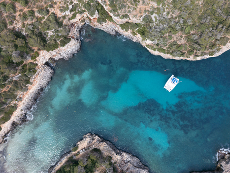 Aerial view of Cala Sa Nau with turquoise waters and a white catamaran anchored near rocky cliffs Felanitx Balearic Islands Spain. Aerial view of Cala Sa Nau with turquoise waters and a white catamaran anchored near rocky cliffs Felanitx Balearic Islands Spain.