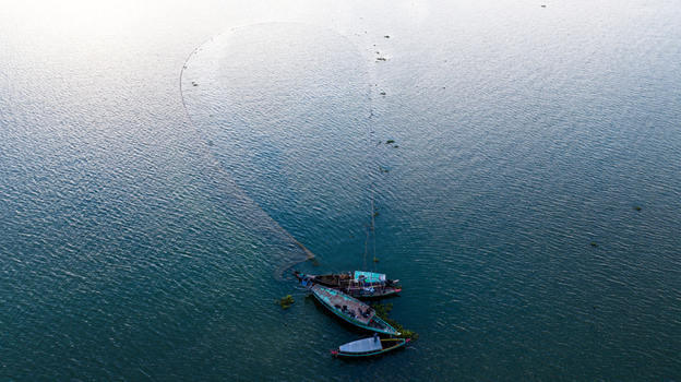 Aerial view of traditional wooden fishing boats on the calm waters of Kaptai Lake with a large circular fishing net deployed in Rangamati Chittagong Division Bangladesh.