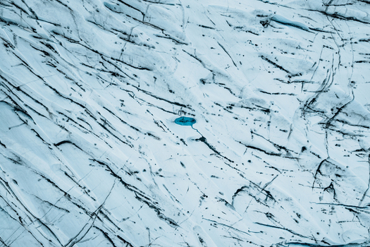 Aerial view of the Vatnajokull glacier featuring deep crevasses and a vibrant blue meltwater pool in Iceland.