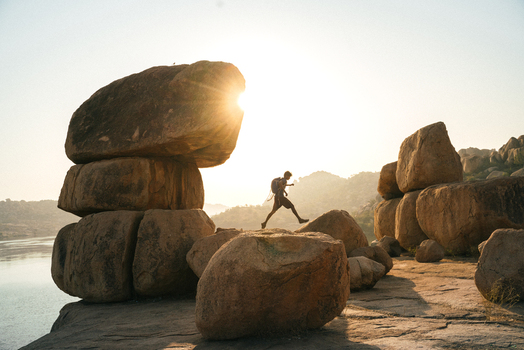 View of a person jumping between large granite boulders during golden hour in the rocky landscape of Hampi Karnataka India. View of a person jumping between large granite boulders during golden hour in the rocky landscape of Hampi Karnataka India.