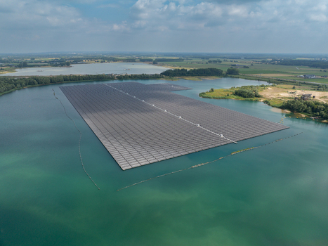 Aerial view of a large floating solar farm on a calm lake surrounded by green fields and trees under a blue sky in the Netherlands. Aerial view of a large floating solar farm on a calm lake surrounded by green fields and trees under a blue sky in the Netherlands.
