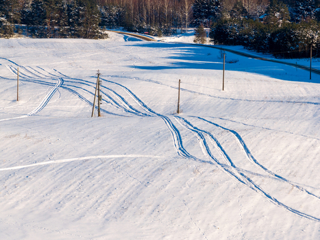 Aerial view of snow covered rolling hills with tire tracks and utility poles near a dense pine forest in Lithuania. Aerial view of snow covered rolling hills with tire tracks and utility poles near a dense pine forest in Lithuania.