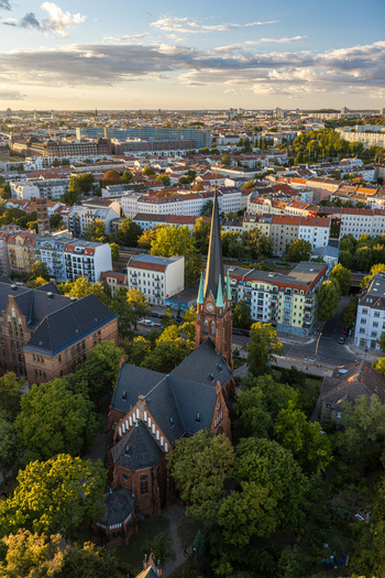 Aerial view of Erloserkirche church surrounded by lush trees and urban residential buildings in the Lichtenberg district during golden hour in Berlin Berlin Germany. Aerial view of Erloserkirche church surrounded by lush trees and urban residential buildings in the Lichtenberg district during golden hour in Berlin Berlin Germany.