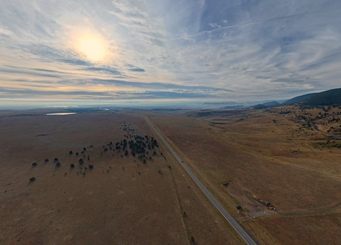 Aerial view of a long highway stretching through the dry grassy plains of the Colorado landscape with scattered trees under a dramatic cloudy sky in Golden Colorado United States.