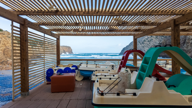 View of Spiaggia di Cala Domestica with pedal boats stored under a wooden pergola overlooking the sea and rocky cliffs in Provincia del Sulcis Iglesiente Sardegna Italy. View of Spiaggia di Cala Domestica with pedal boats stored under a wooden pergola overlooking the sea and rocky cliffs in Provincia del Sulcis Iglesiente Sardegna Italy.