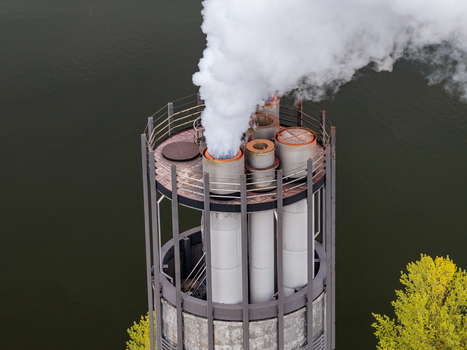 Aerial view of the Klarwerk Ruhleben industrial chimney emitting white steam with surrounding lush green trees and dark water in Berlin Berlin Germany.