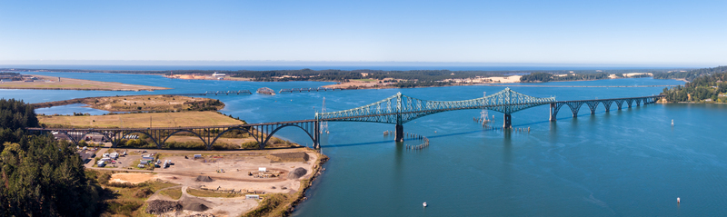 Aerial view of the McCullough Memorial Bridge spanning the Coos Bay with surrounding lush green landscape calm blue water and clear sky in North Bend Oregon United States. Aerial view of the McCullough Memorial Bridge spanning the Coos Bay with surrounding lush green landscape calm blue water and clear sky in North Bend Oregon United States.