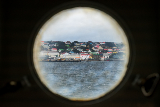 View of the colorful houses and harbor of Stanley seen through a circular porthole in Stanley East Falkland Falkland Islands.