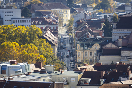 View of a street cuts through buildings and colorful trees cars line the road in the city center on a sunny day Graz Styria Austria. View of a street cuts through buildings and colorful trees cars line the road in the city center on a sunny day Graz Styria Austria.