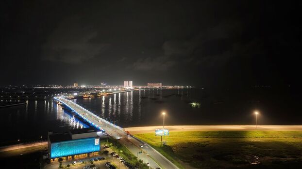 Aerial view of the illuminated Pantai Indah Kapuk 2 bridge over dark water at night with glowing buildings and coastal infrastructure in Kecamatan Penjaringan Banten Indonesia. Aerial view of the illuminated Pantai Indah Kapuk 2 bridge over dark water at night with glowing buildings and coastal infrastructure in Kecamatan Penjaringan Banten Indonesia.