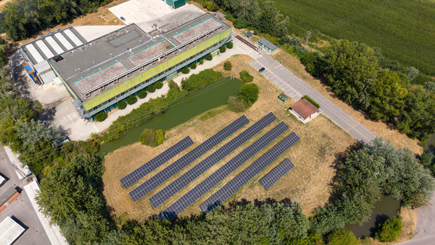 Aerial view of a solar farm featuring rows of photovoltaic panels an industrial building a small pond and surrounding greenery in Tavazzano con Villavesco Lombardy Italy.