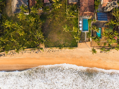 Aerial view of luxury villas with swimming pools and solar panels nestled among palm trees along a sandy beach with crashing waves Galle Southern Province Sri Lanka. Aerial view of luxury villas with swimming pools and solar panels nestled among palm trees along a sandy beach with crashing waves Galle Southern Province Sri Lanka.