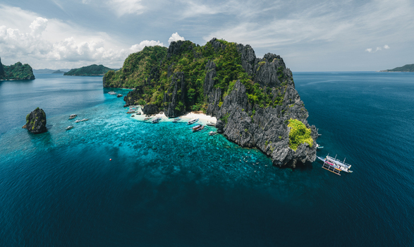 Aerial view of the limestone cliffs and turquoise waters featuring traditional outrigger boats moored near the white sand beach in El Nido Mimaropa Philippines. Aerial view of the limestone cliffs and turquoise waters featuring traditional outrigger boats moored near the white sand beach in El Nido Mimaropa Philippines.