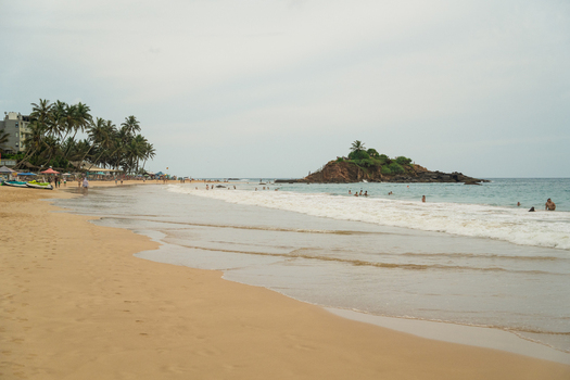 View of Mirissa Beach with people swimming near Parrot Rock and palm trees lining the shore in Mirissa Southern Province Sri Lanka. View of Mirissa Beach with people swimming near Parrot Rock and palm trees lining the shore in Mirissa Southern Province Sri Lanka.