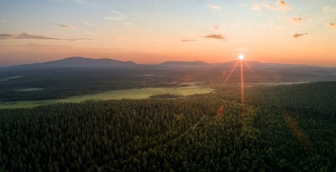 Aerial view of the Neitokainen lake area surrounded by vast coniferous forests and distant mountains under a golden sunset in Kittila Lapland Finland. Aerial view of the Neitokainen lake area surrounded by vast coniferous forests and distant mountains under a golden sunset in Kittila Lapland Finland.